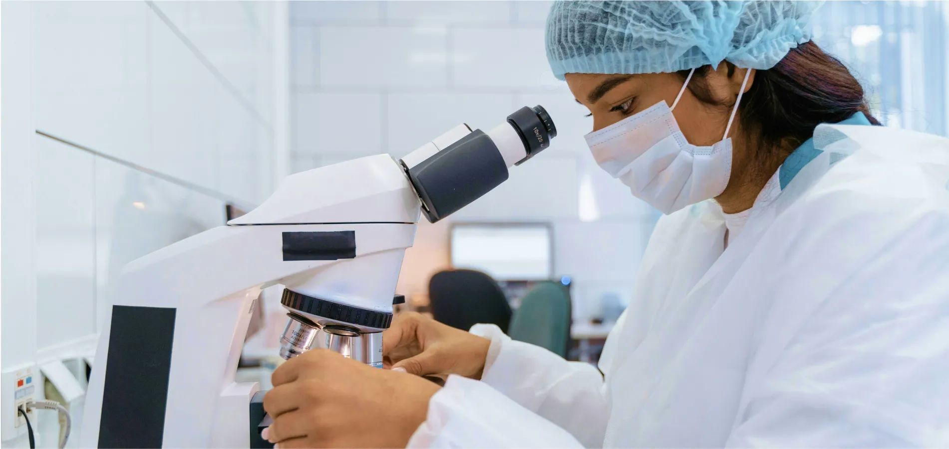 Una técnica de laboratorio mirando una muestra con un microscopio en un laboratorio
