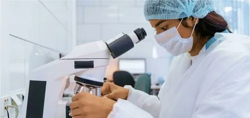 Una técnica de laboratorio mirando una muestra con un microscopio en un laboratorio